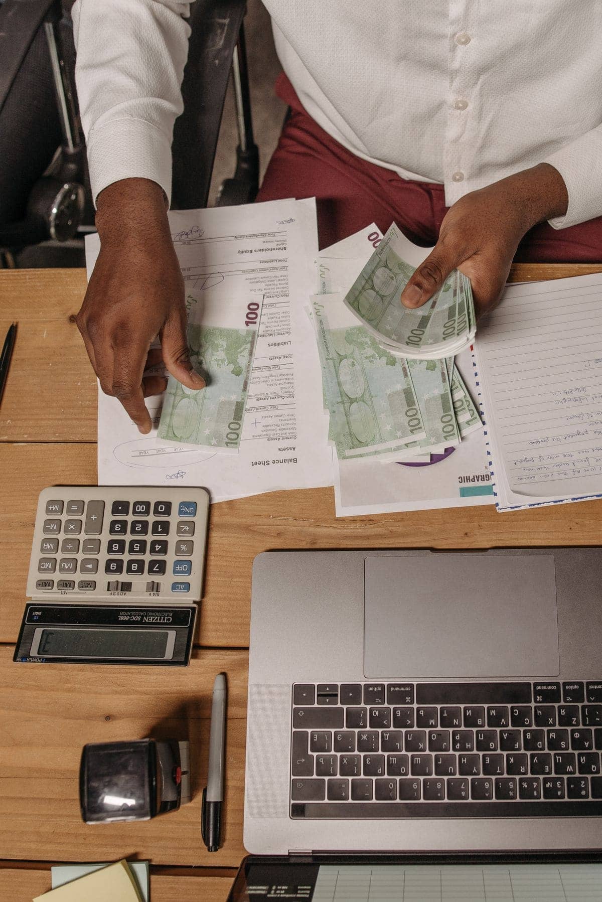 Person counting cash and using a calculator on a desk