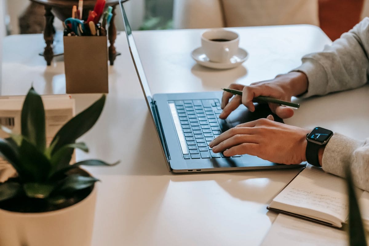 Freelancer working on a laptop at a home desk, with coffee and a notebook